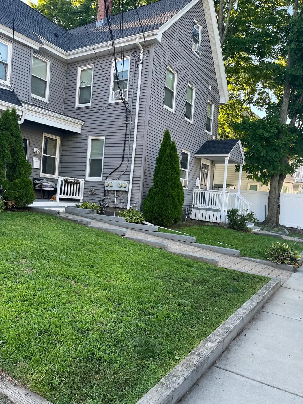 A trimmed front lawn beside a paver walkway and clipped arborvitae